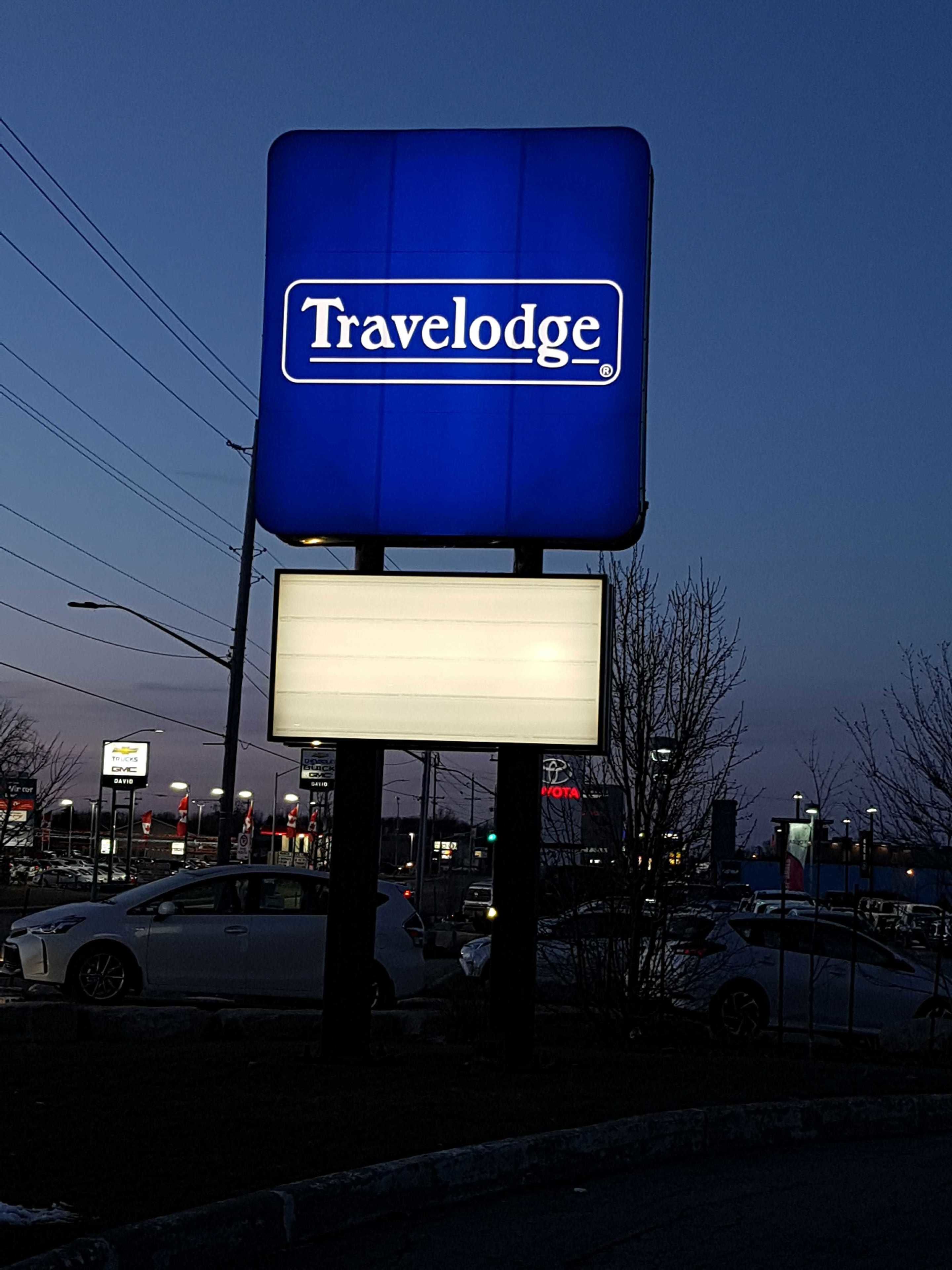 A Travelodge sign with a blank lower panel, surrounded by a parking lot with cars and streetlights.