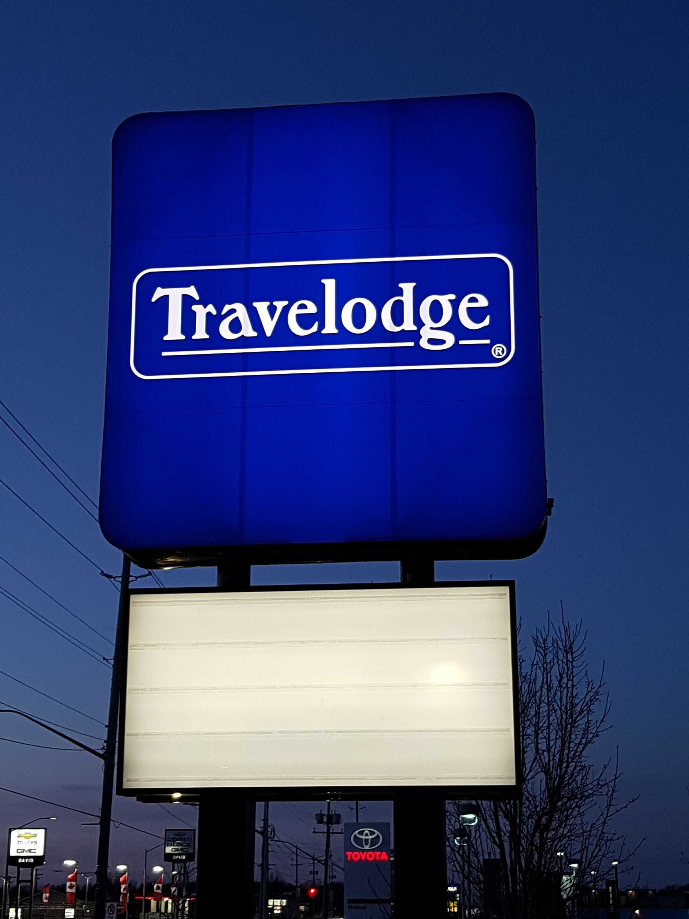 A Travelodge sign with a large illuminated blue signboard and a blank white sign below it.