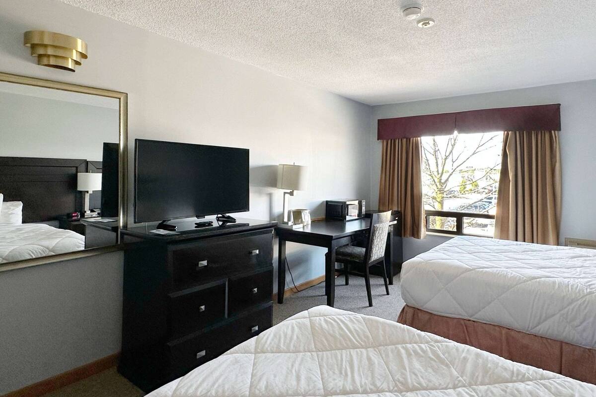Habitación de hotel con dos camas, un escritorio con televisor, cómoda y ventana con cortinas.