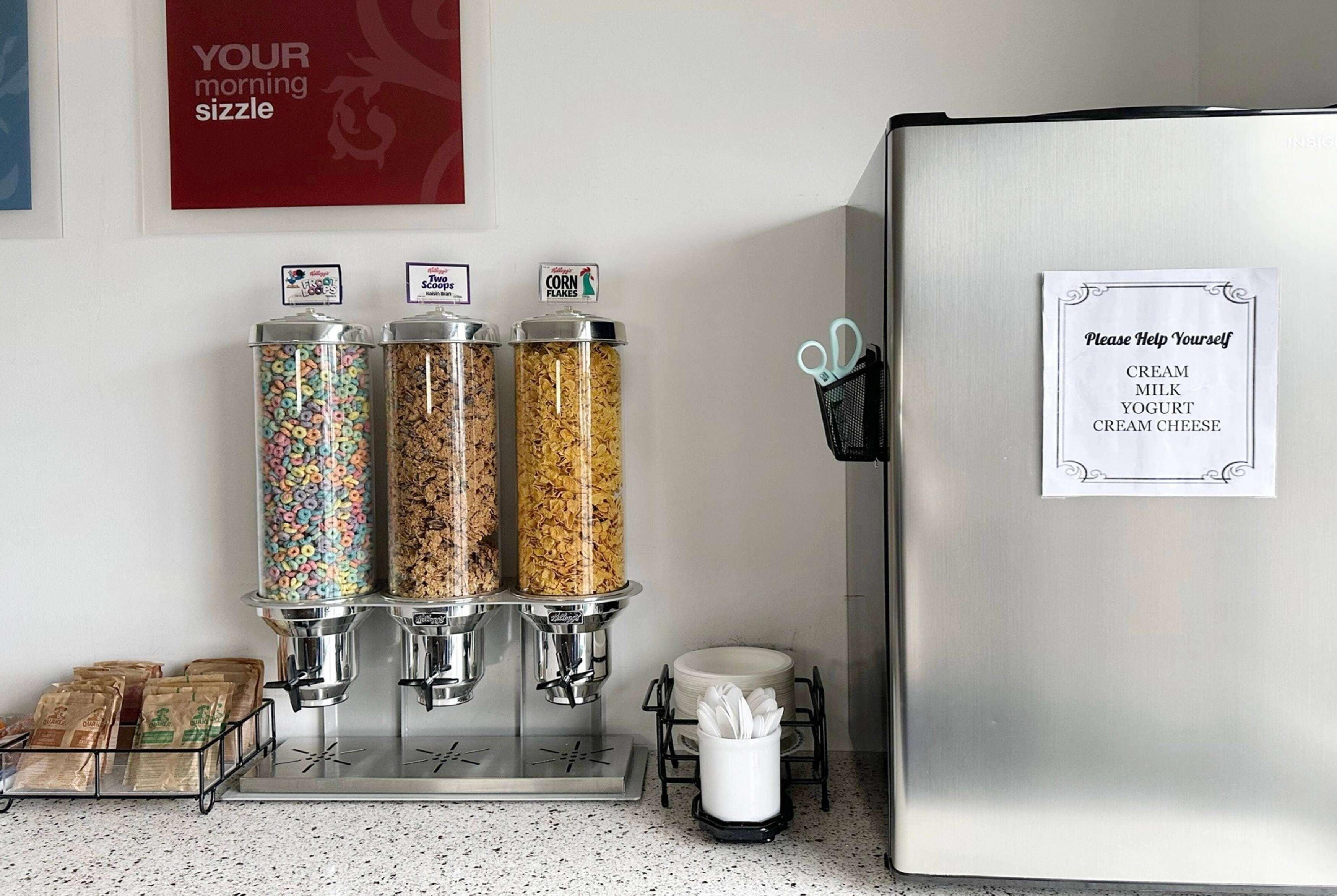A breakfast bar with cereal dispensers, a coffee machine, and a sign instructing to help oneself.