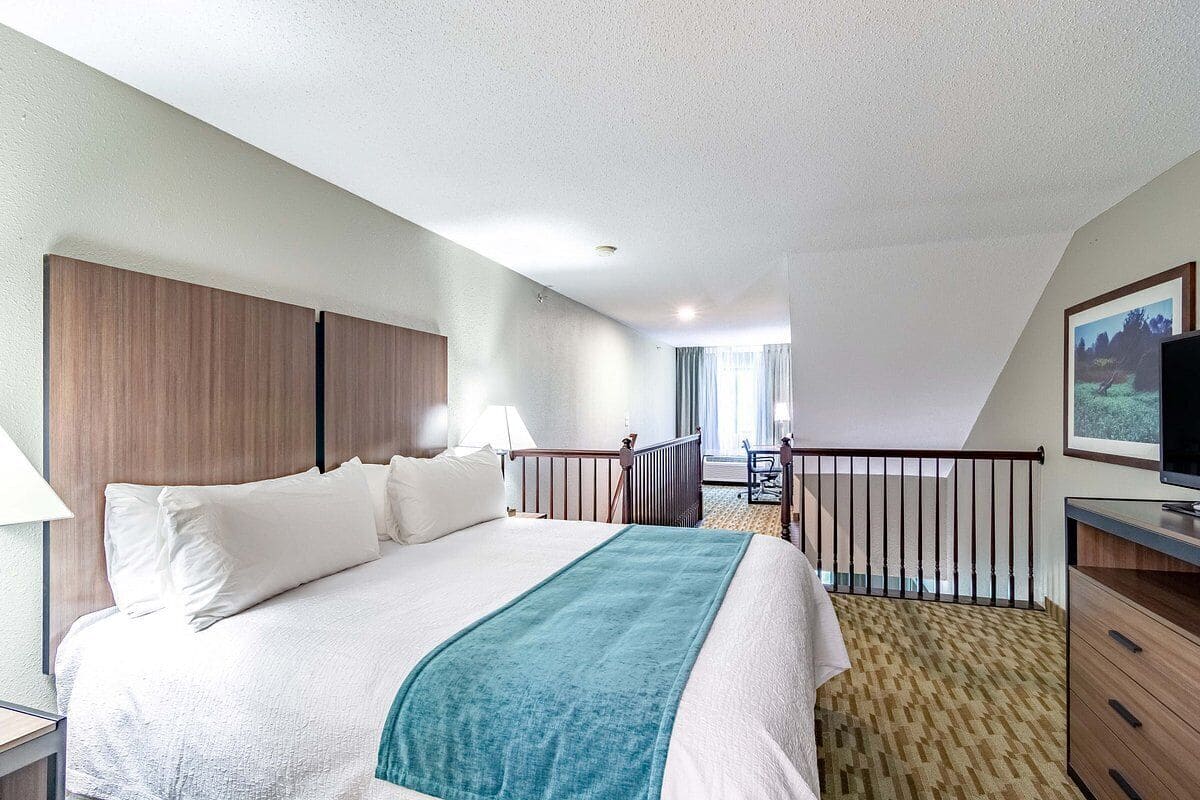 A hotel room with a bed, a desk, a chair, a TV, and a balcony with a railing.