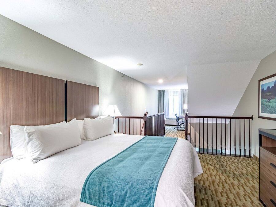 A hotel room with a bed, a desk, a chair, a TV, and a balcony with a railing.
