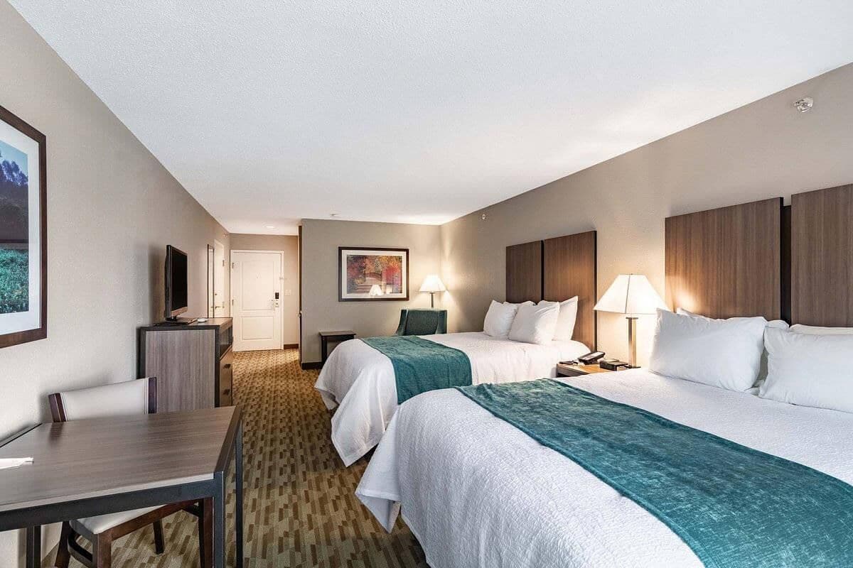 A hotel room with two beds, a desk, a TV, and a painting on the wall.