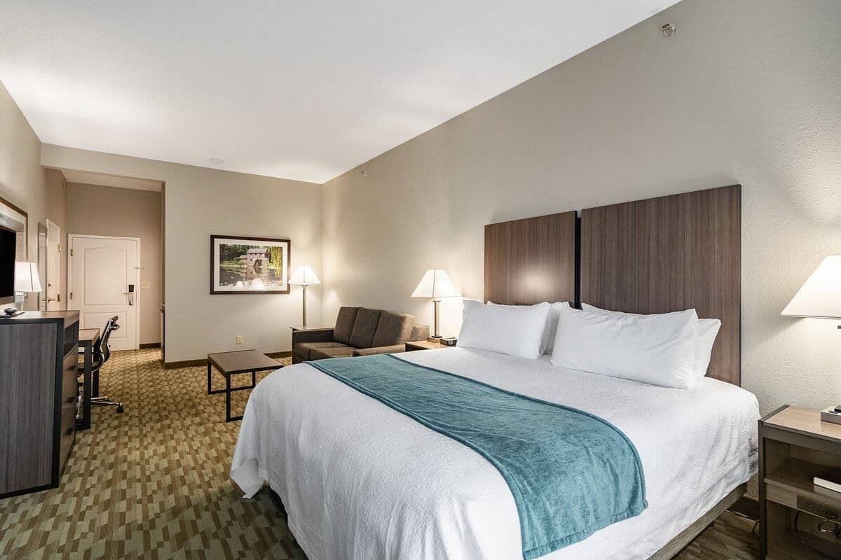 A hotel room with a bed, desk, chair, lamps, and a framed picture on the wall.