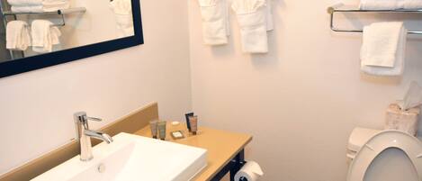 A bathroom with a sink, mirror, towel rack, toilet, and a roll of toilet paper.