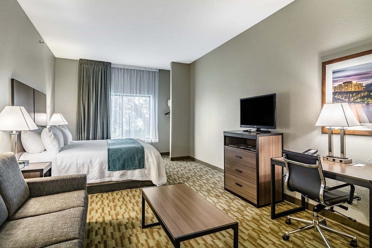 A hotel room with a bed, a desk, a chair, a television, and a window with curtains.
