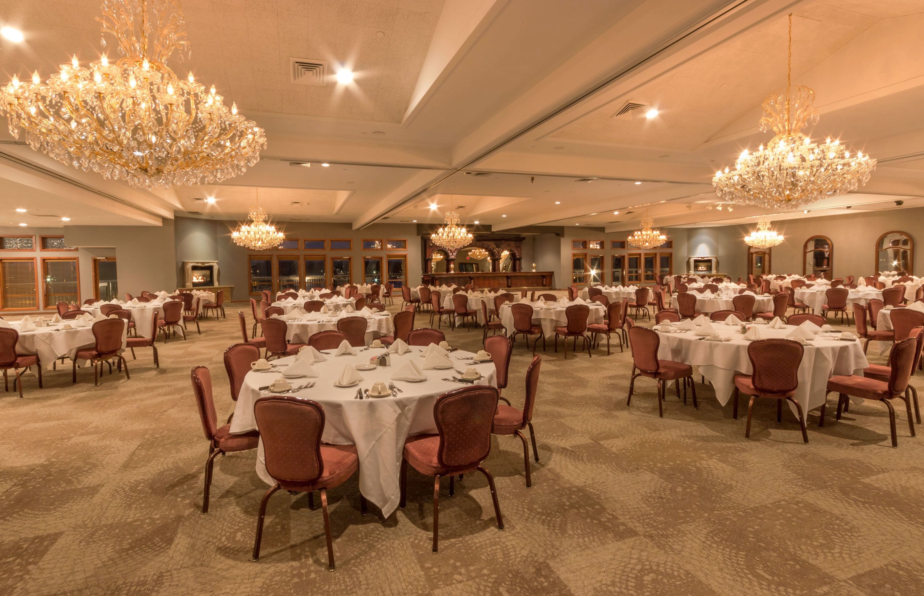 Un amplio salón de banquetes con mesas redondas dispuestas para cenar, candelabros y una zona de bar.