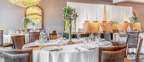 A banquet hall with round tables, chandeliers, and draped curtains.