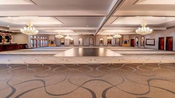 A spacious hall with chandeliers, a patterned carpet, and framed artwork on the walls.