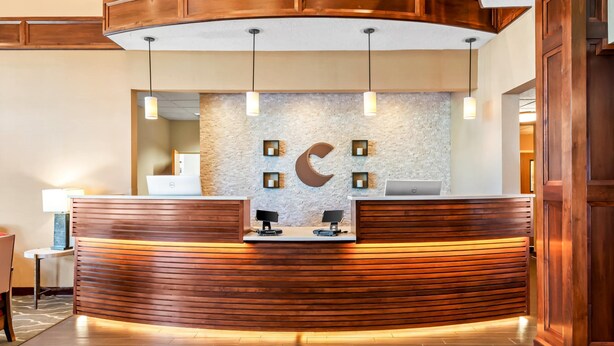 A reception desk with a wooden finish, a stone wall with a crescent moon design, and a laptop on the counter. - Comfort Suites Linn County (Albany)