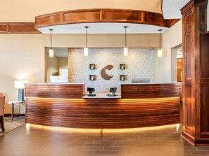 A reception desk with a wooden finish, a stone wall with a crescent moon design, and a laptop on the counter. - Comfort Suites Linn County (Albany)