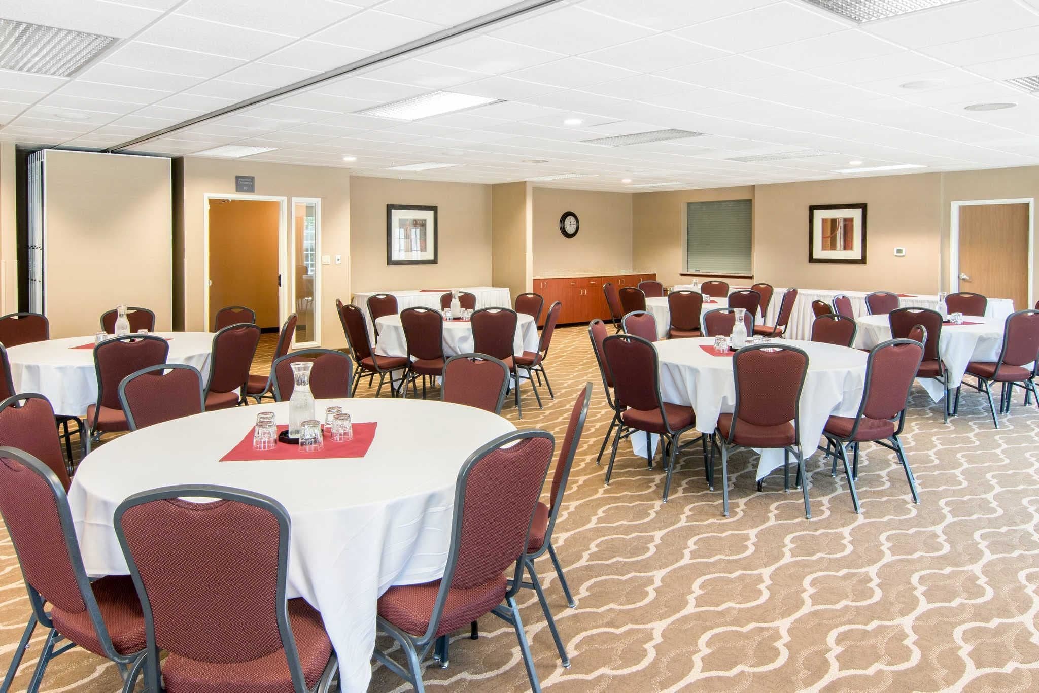 A conference room with multiple round tables, each with a white tablecloth and red chairs.