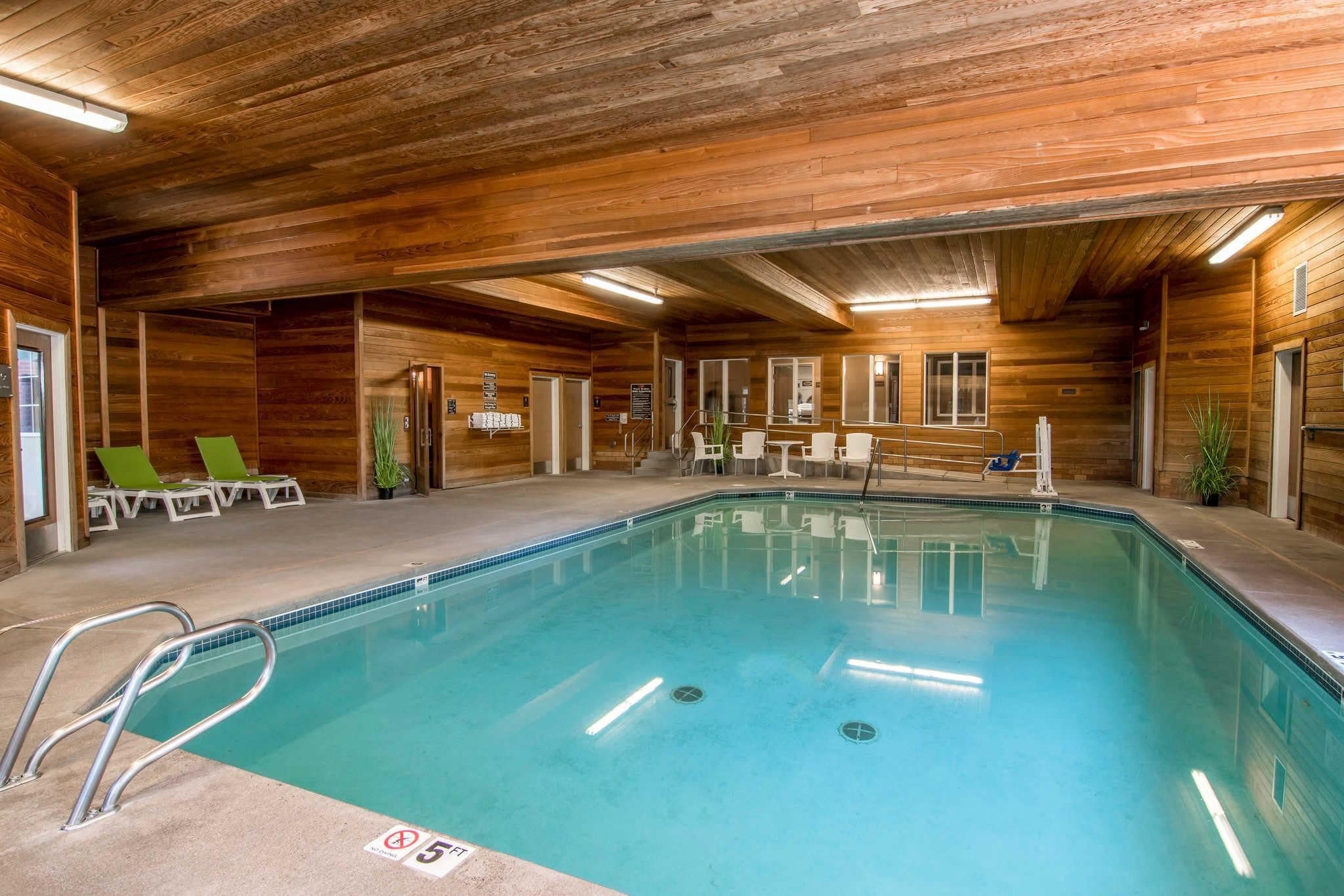 An indoor swimming pool with wooden walls, lounge chairs, and a lifeguard stand.