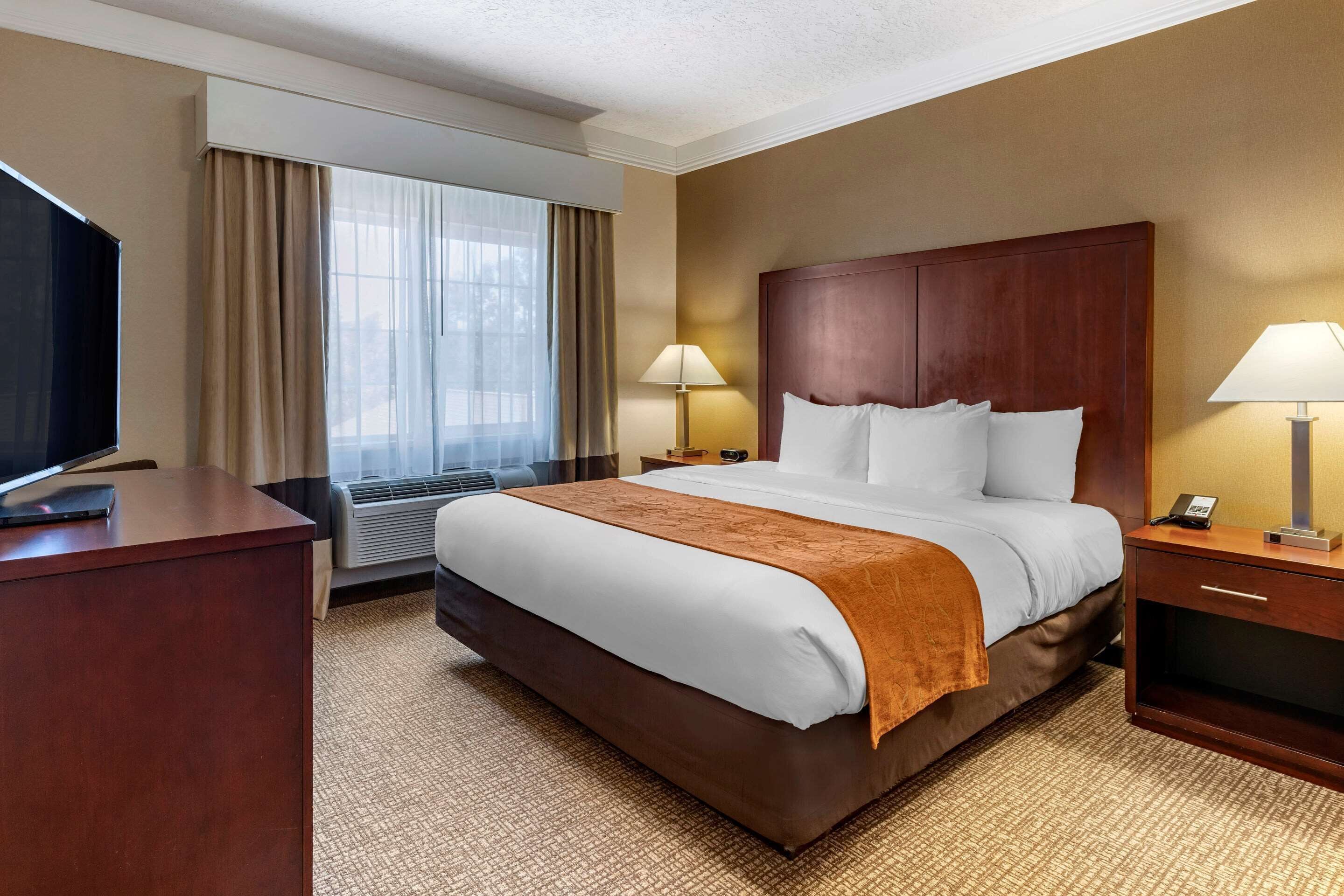 A hotel room with a large bed, two bedside tables with lamps, a TV on a desk, and a window with curtains.