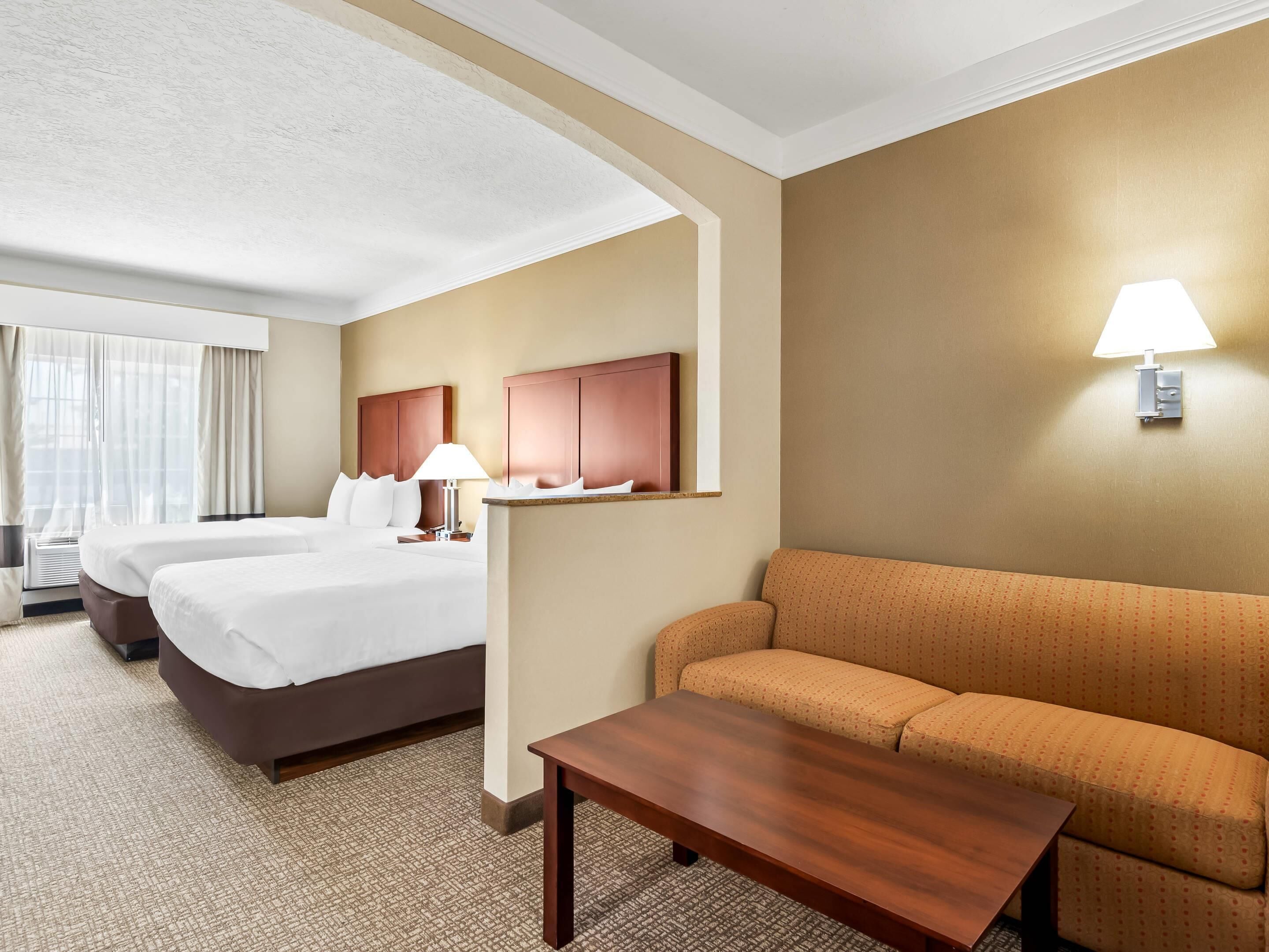 A hotel room with two beds, a sofa, a small table, and a lamp.