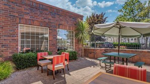 An outdoor patio with brick walls, large windows, and outdoor seating including tables and chairs. - Comfort Suites Linn County (Albany)