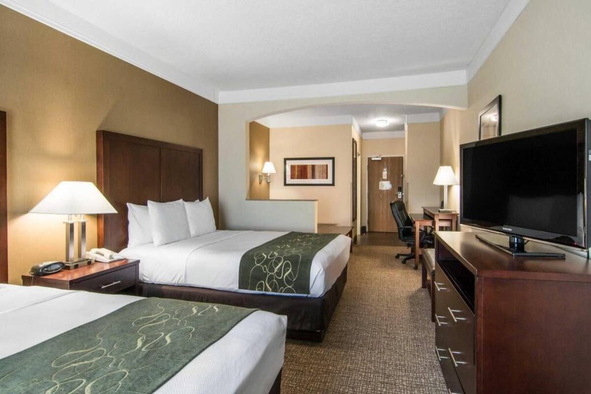 A hotel room with two beds, a desk with a TV, and a chair.