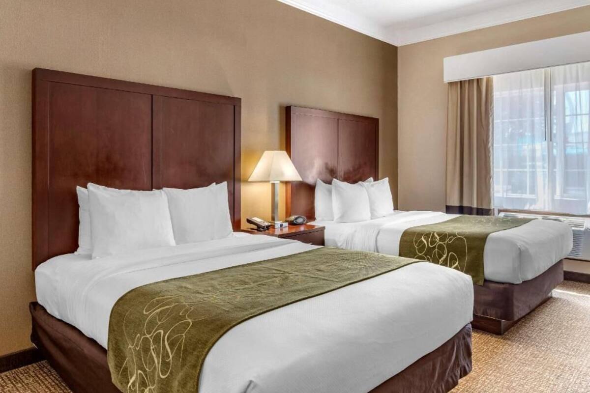 A hotel room with two beds, a nightstand with a lamp, and a window with curtains.