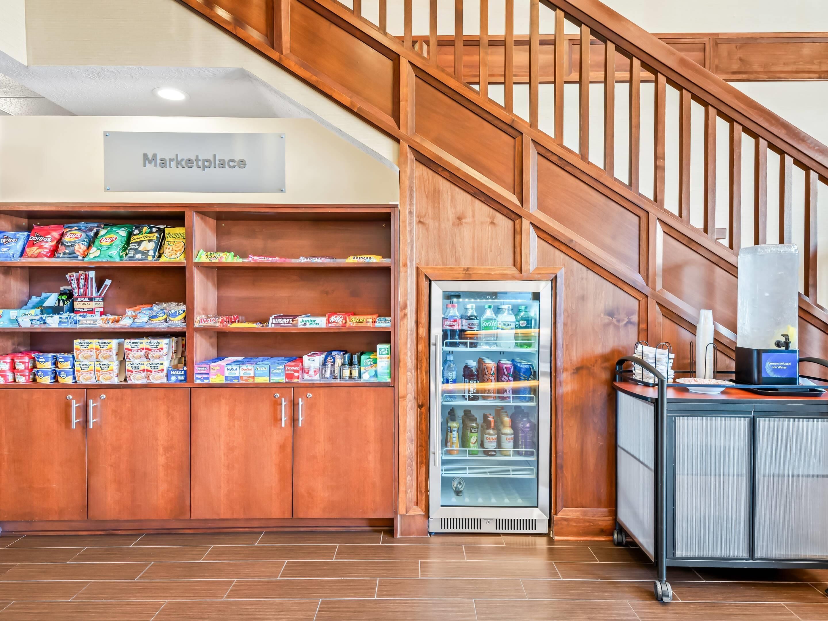 Una kitchenette con un refrigerador lleno de bebidas, una cafetera y diversos alimentos.