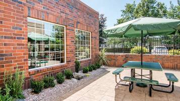 A brick building with large windows and a patio area with picnic tables and an umbrella.