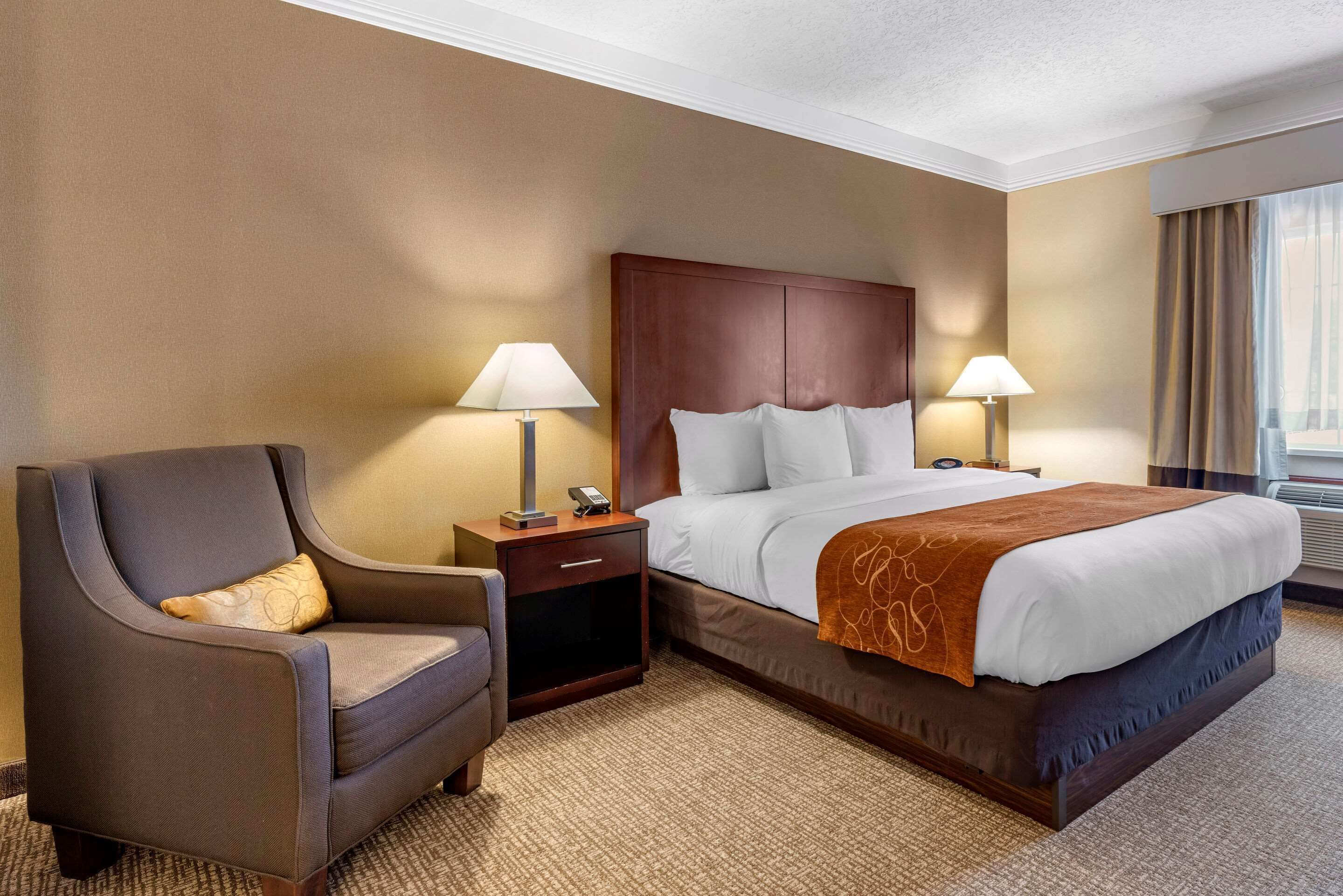 A hotel room with a large bed, a chair, two bedside tables with lamps, and a window with curtains.