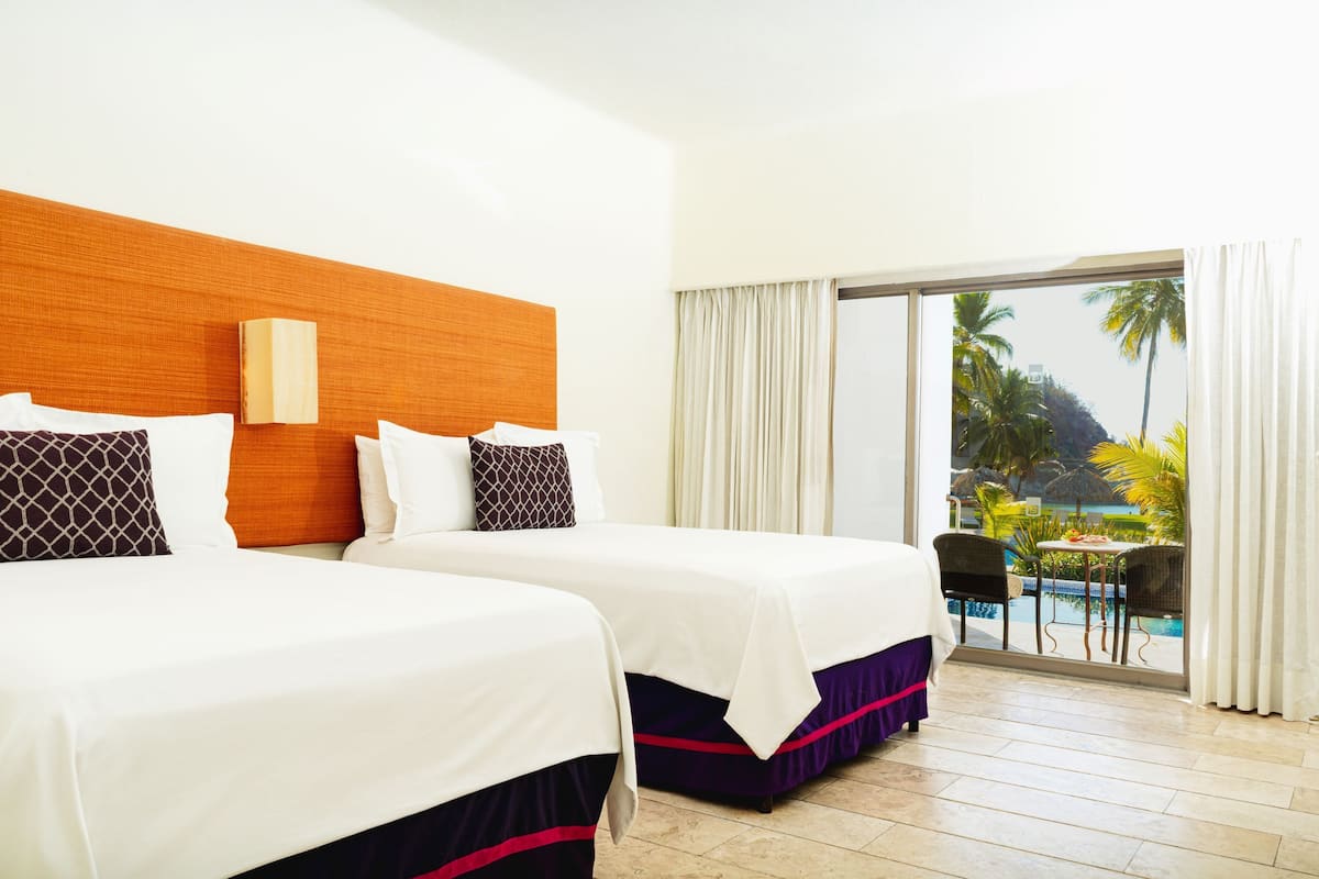 Ein Hotelzimmer mit zwei Betten, einem hölzernen Kopfteil, einem großen Fenster mit Blick auf einen Pool und Palmen sowie einer Schiebeglastür.