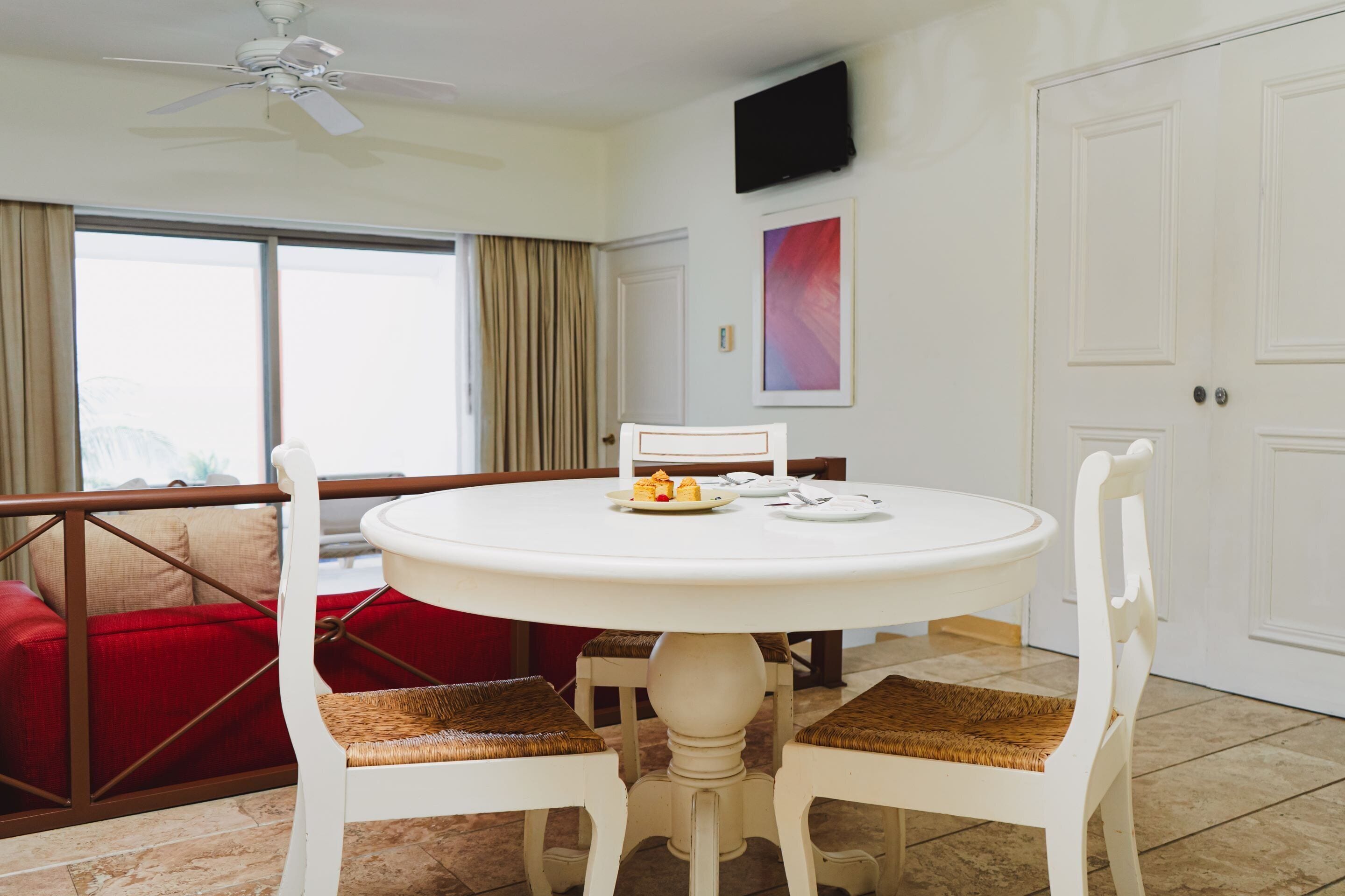 A dining area with a round table, white chairs, and a red couch.