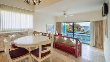 A hotel room with a dining area, a red sofa, a ceiling fan, and a view of the ocean.