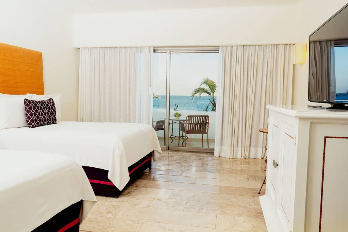 Ein Hotelzimmer mit zwei Betten, einem Fernseher, einem Schreibtisch und Blick aufs Meer.