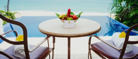 Una mesa con frutero y una tarjeta, con vista a la playa y la piscina.