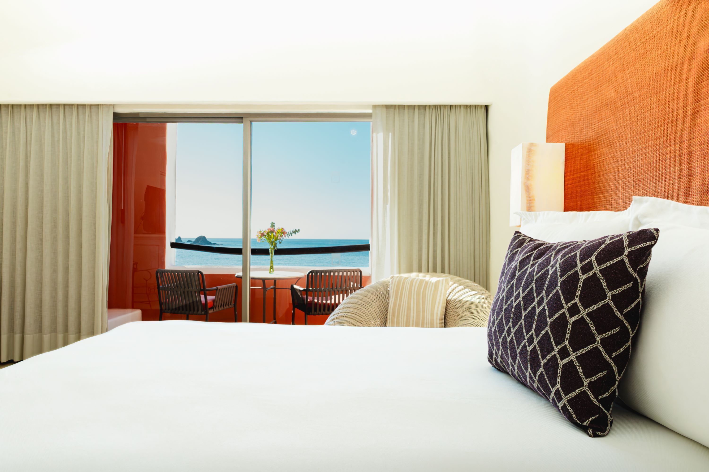 Ein Hotelzimmer mit einem großen Bett, Meerblick und einem Balkon mit Stühlen und einem Tisch.