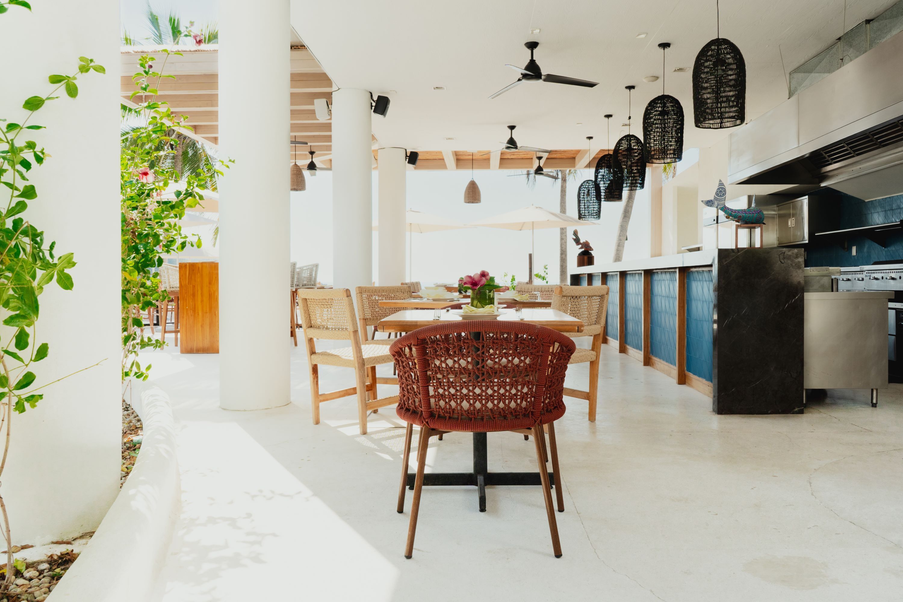 Cocina y comedor de concepto abierto con techos altos, luces colgantes y una mesa de comedor central rodeada de sillas de mimbre.