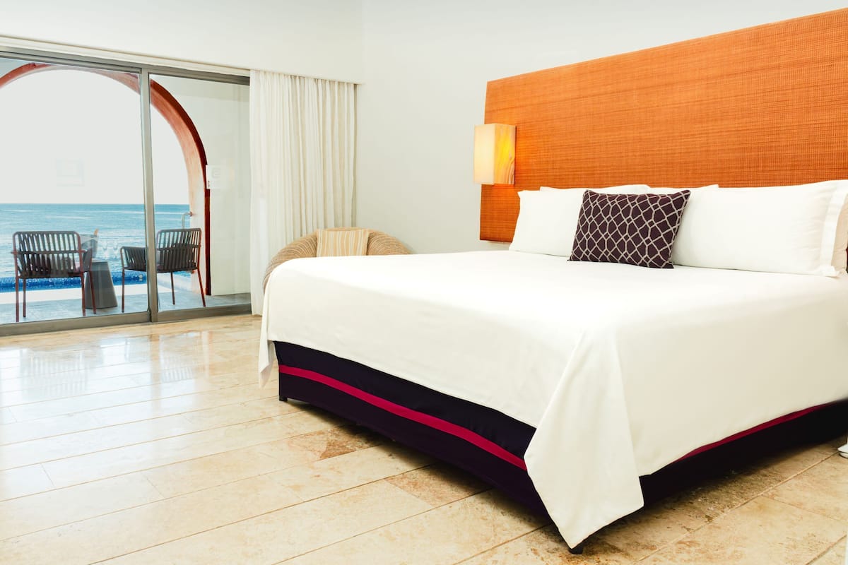 Ein Hotelzimmer mit einem großen Bett, Meerblick, einer Schiebetür und einer Sitzecke mit Stühlen.