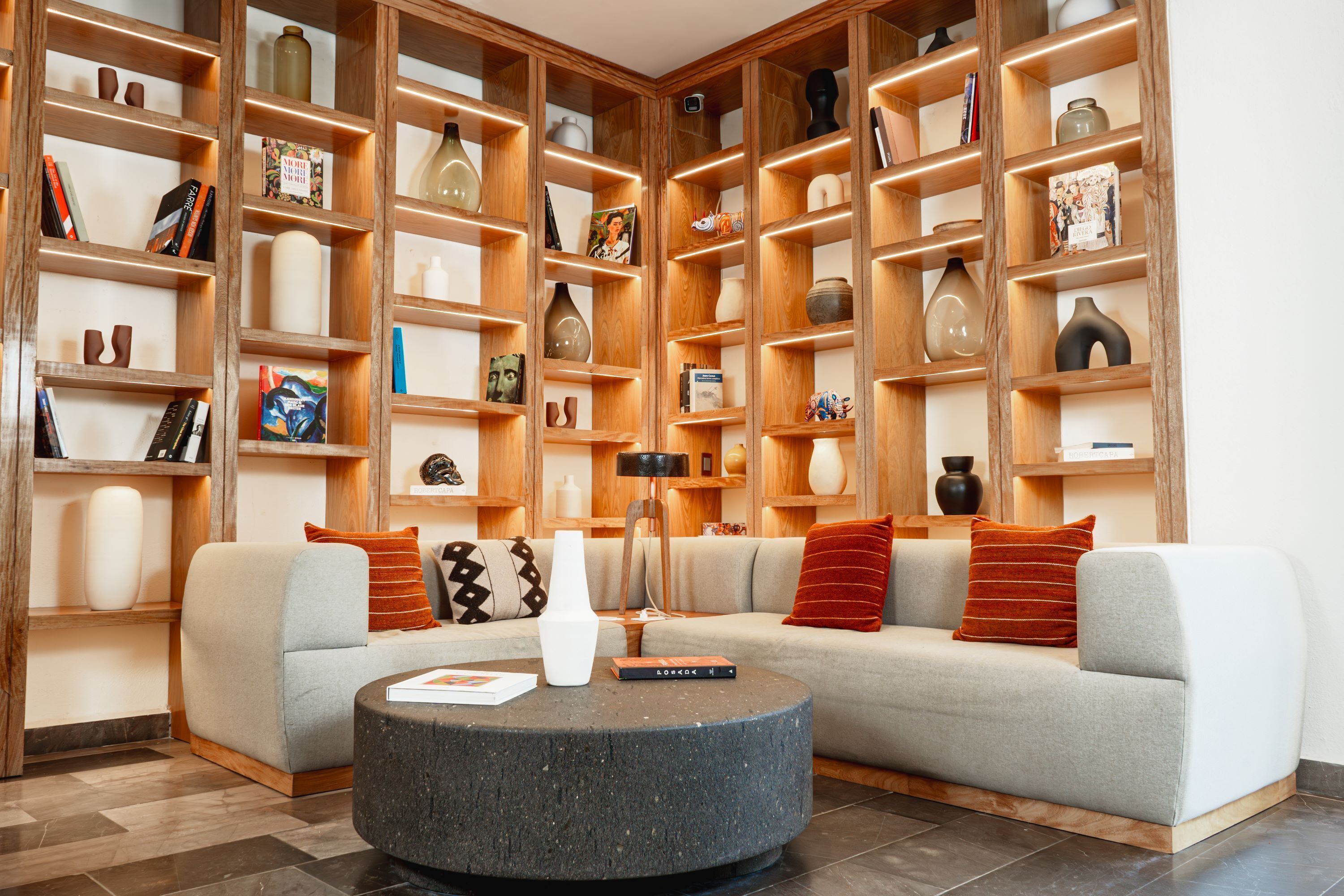 Una sala de estar moderna con un sofá modular, una mesa de centro redonda y estanterías de madera decoradas con objetos ornamentales.