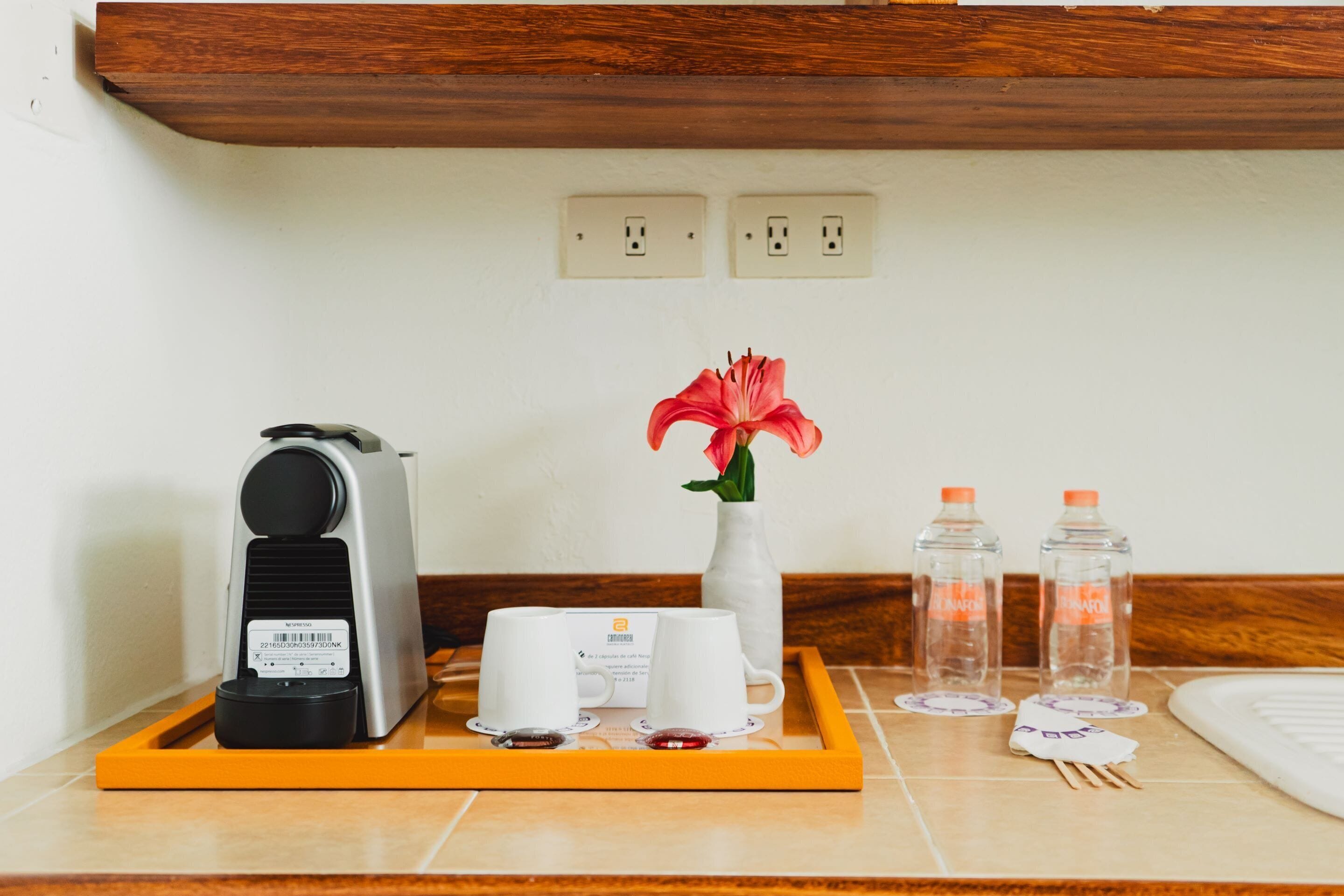 A hotel room's breakfast tray with a coffee maker, two white cups, a vase with a red flower, and two water bottles.