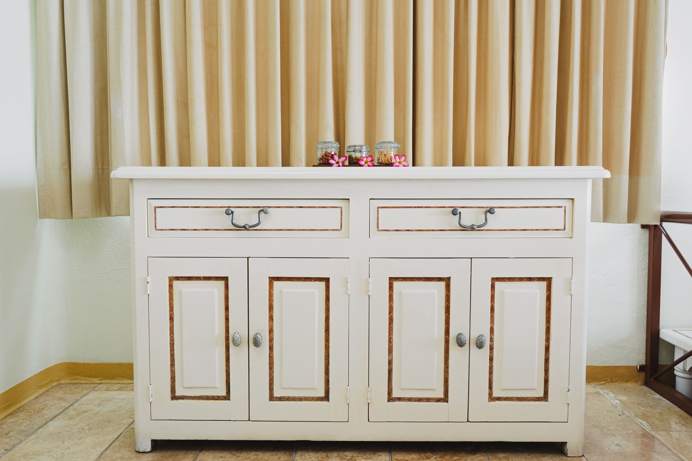 A white cabinet with two drawers and two doors, topped with jars and flowers.