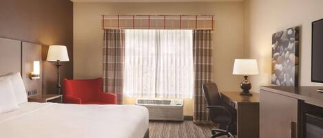 A hotel room with a large bed, a desk with a chair, a TV, and a window with curtains.