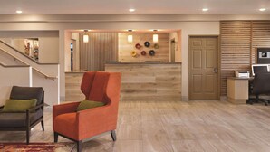 A modern lobby with a wooden reception desk, a staircase, and a seating area with two chairs. - Country Inn & Suites by Radisson, Albert Lea - Austin (Albert Lea)