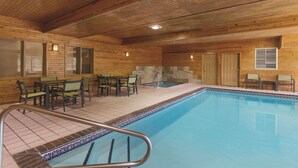 An indoor swimming pool with wooden walls and tiled flooring, surrounded by seating areas and doors. - Country Inn & Suites by Radisson, Albert Lea - Austin (Albert Lea)