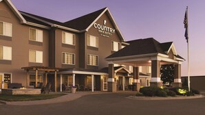 A Country Inn & Suites building with a covered entrance, multiple windows, and a flagpole. - Country Inn & Suites by Radisson, Albert Lea - Austin (Albert Lea)