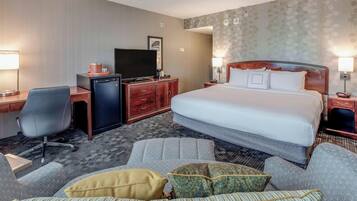 A hotel room with a large bed, a desk with a television, a chair, and a sofa with cushions.
