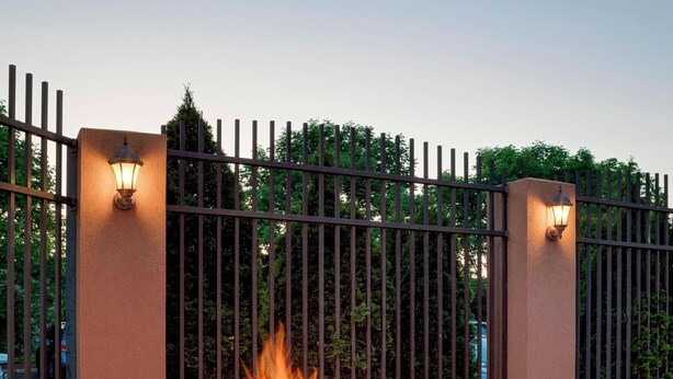 A circular stone fire pit with a fire, surrounded by wicker furniture and a metal fence. - Courtyard by Marriott Cranbury South Brunswick (Cranbury)