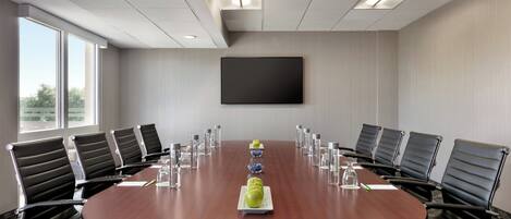 Une salle de conférence équipée d’une table ronde, de fauteuils en cuir noir et d’un grand téléviseur à écran plat fixé au mur.