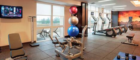 Un gimnasio con equipo de ejercicio, un televisor y ventanas amplias.