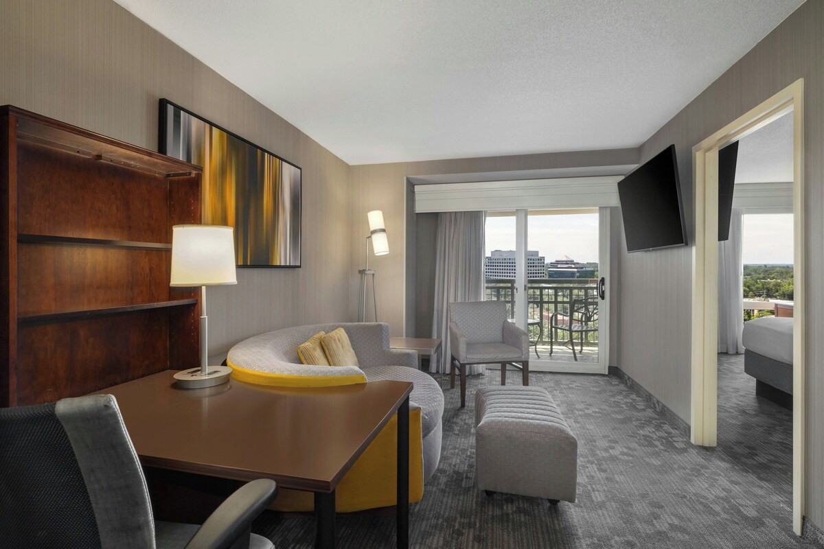 A hotel room with a dining area, a sofa, a TV, and a balcony with a view.