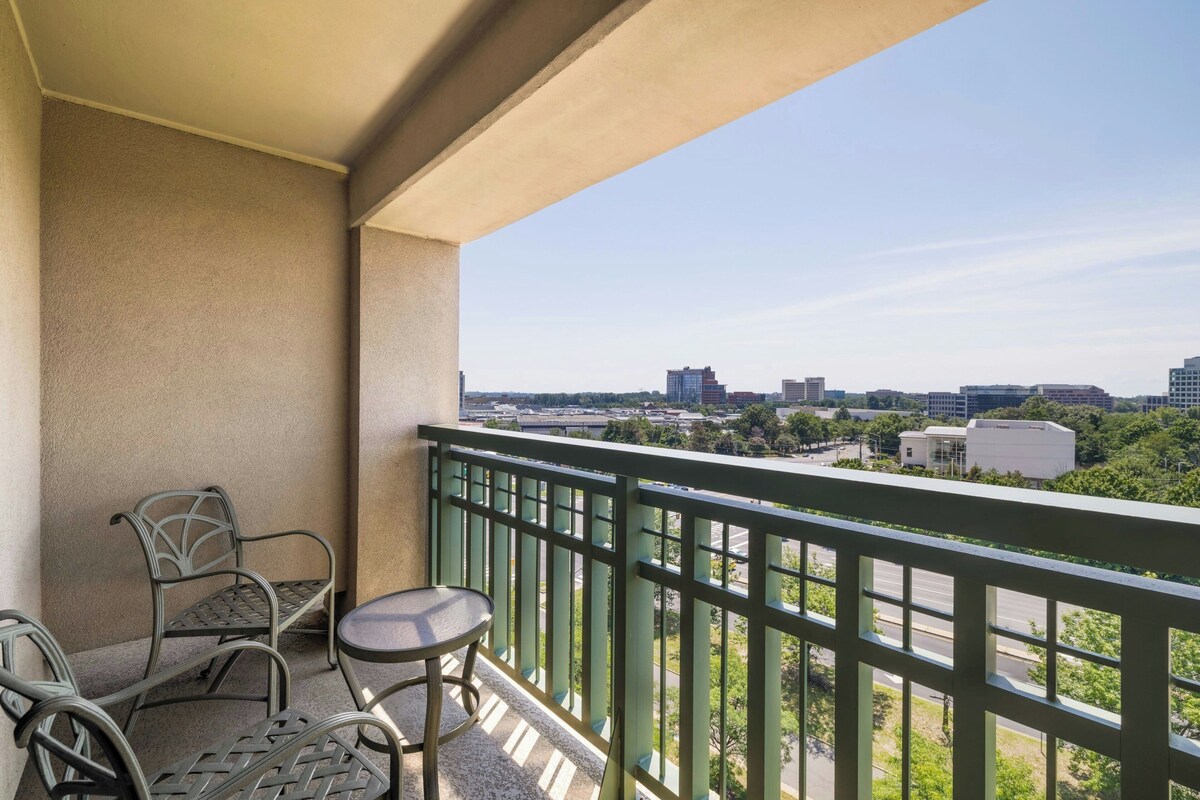 A balcony with a view of a cityscape, featuring a table and chairs.
