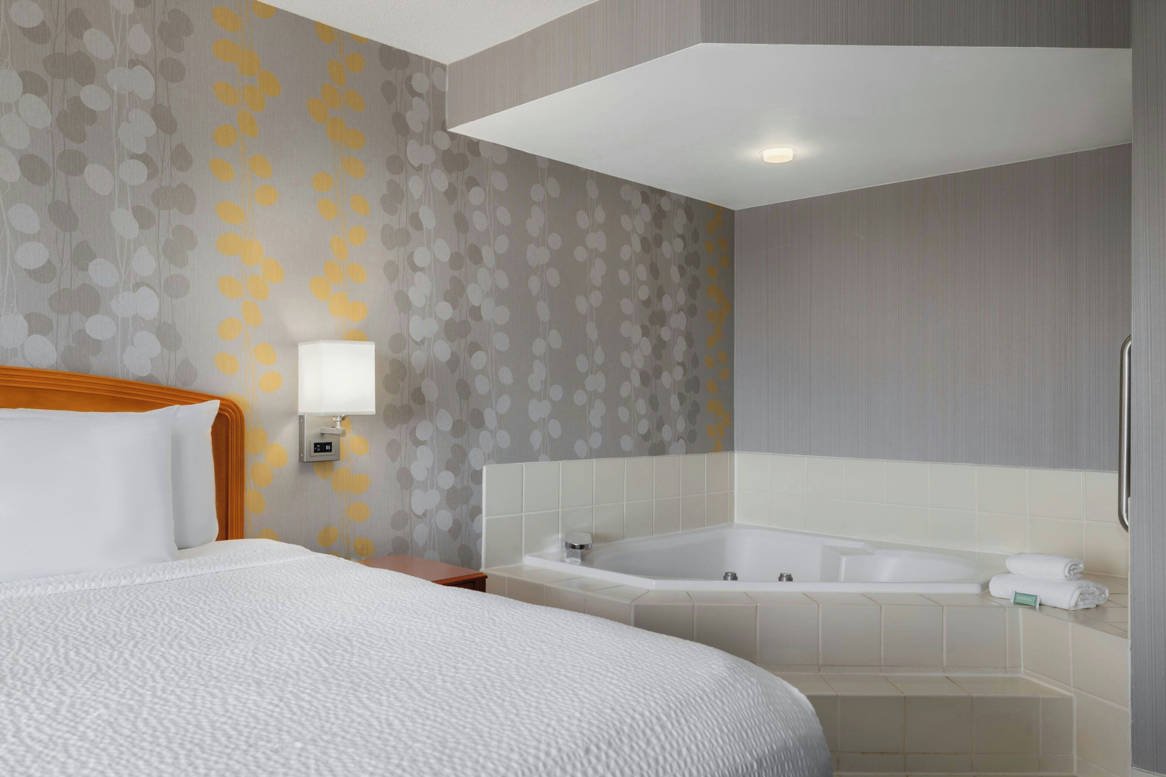 Habitación de hotel con una cama grande, un baño con bañera y una lámpara fijada a la pared.