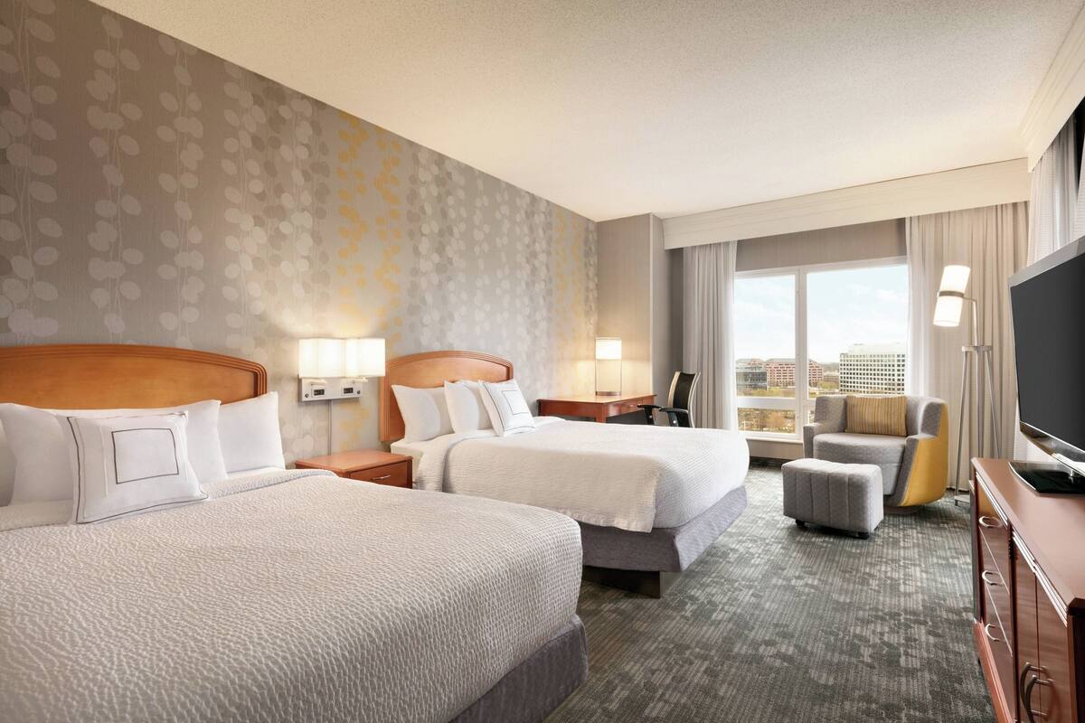 A hotel room with two beds, a sofa, a TV, and a city view.