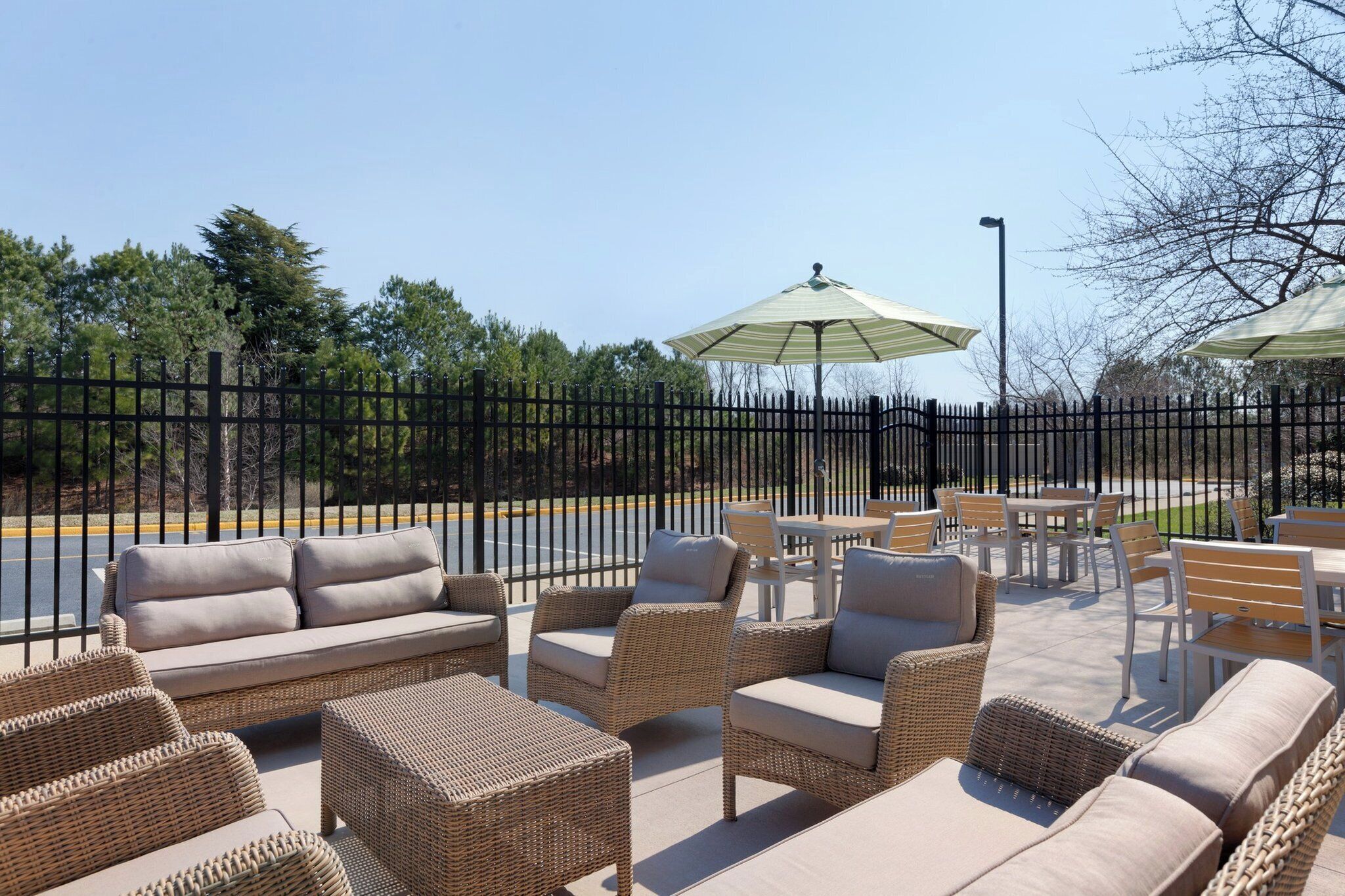Outdoor seating with wicker furniture and a table, a fenced area, and a view of trees and a road.