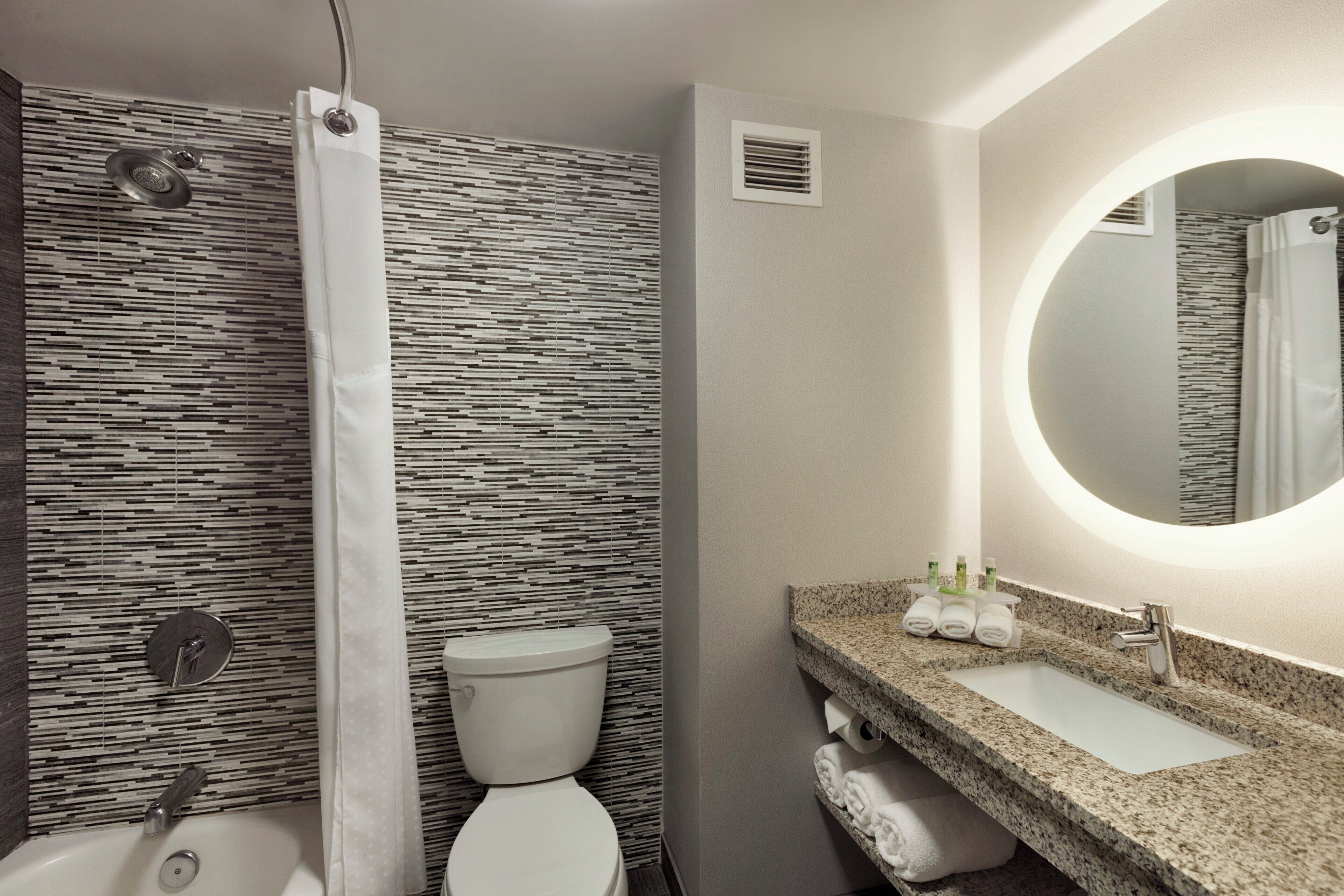 A bathroom with a shower, toilet, sink, and a mirror.